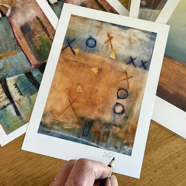 Signing Signed art prints spread across a worktable as the artist prepares affordable 5x7 prints for Open Studios.