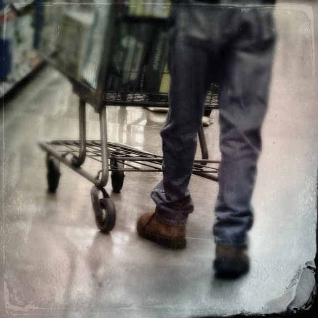 An old man pushing a grocery cart as seen from behind